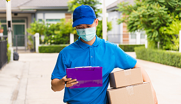 man carrying boxes under his arm checking a clipboard with his other arm